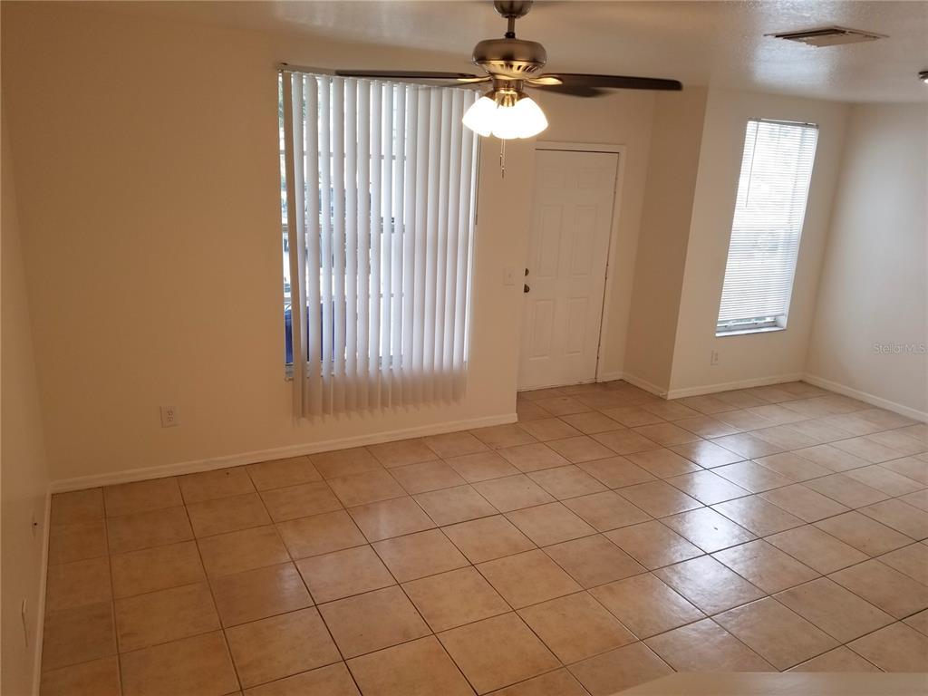 An empty room features beige tile flooring, a ceiling fan, and vertical blinds on windows — 6116 OLIVEDALE DRIVE, RIVERVIEW, FL
