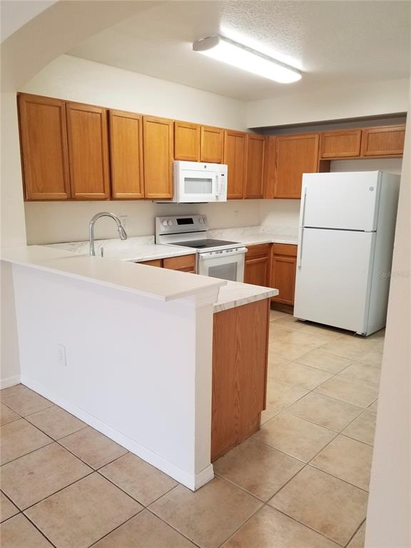 A kitchen features wood cabinets, white appliances, a breakfast bar, and light-colored tile flooring — 6116 OLIVEDALE DRIVE, RIVERVIEW, FL