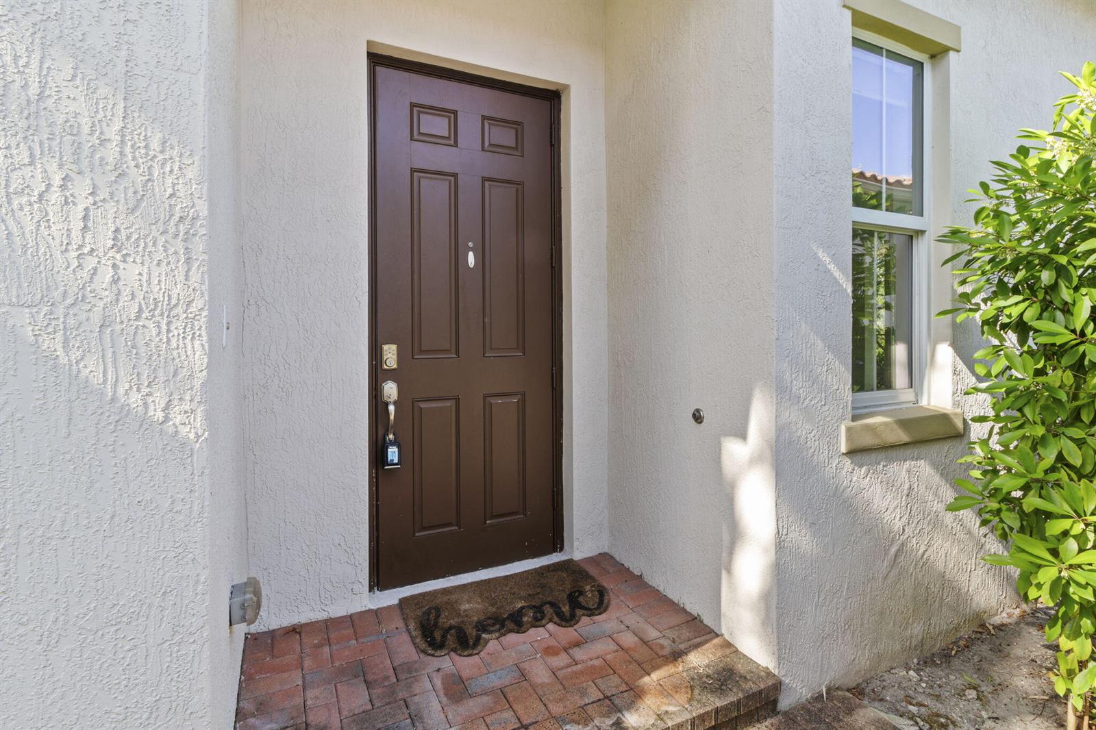 A brown front door with a lockbox sits on a brick porch beside a window — 5319 Falcon Trail, Davie FL 33314, DAVIE, FL