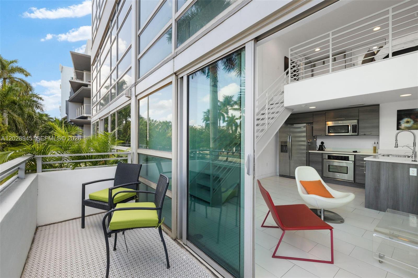 A balcony with two chairs overlooks a modern kitchen and living area with a staircase — 421 Meridian Ave # 6, Miami Beach FL 33139, MIAMI BEACH, FL