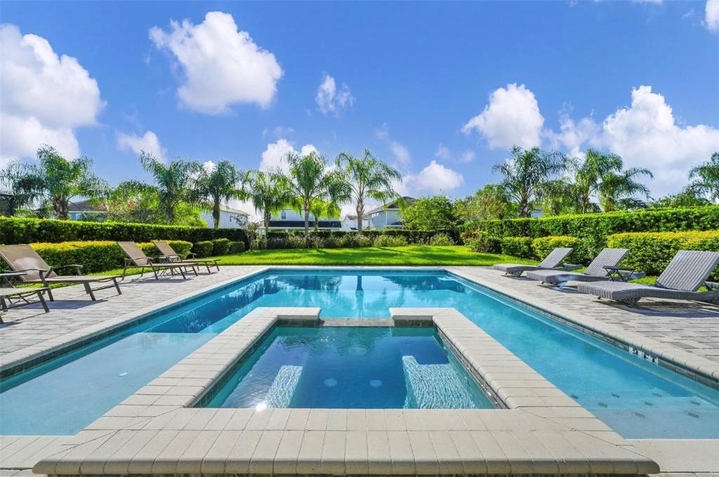 A rectangular swimming pool with an integrated spa is surrounded by lounge chairs and landscaping — 7727 FAIRFAX DRIVE, KISSIMMEE, FL