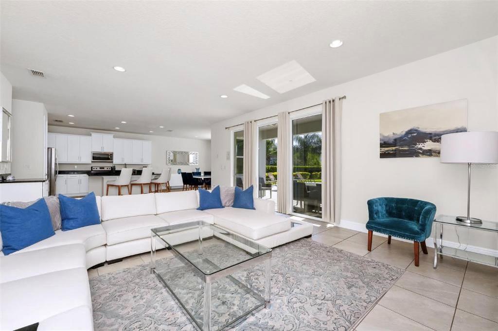 A bright living room features a white sectional sofa, blue accents, and an open kitchen — 7727 FAIRFAX DRIVE, KISSIMMEE, FL