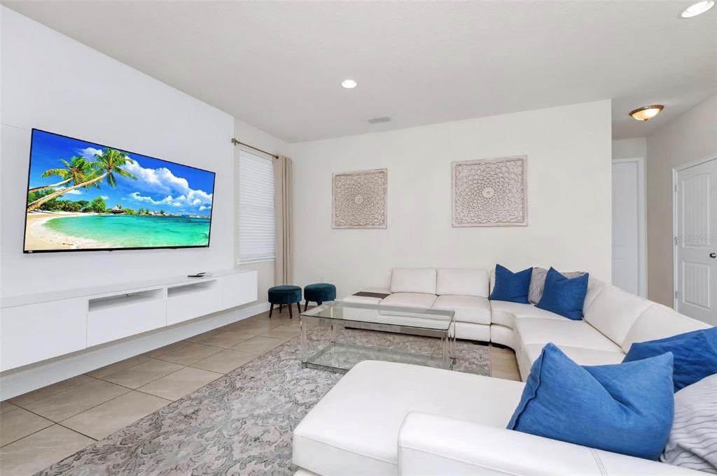 A modern living room features a white sectional sofa, glass coffee table, and wall-mounted television — 7727 FAIRFAX DRIVE, KISSIMMEE, FL