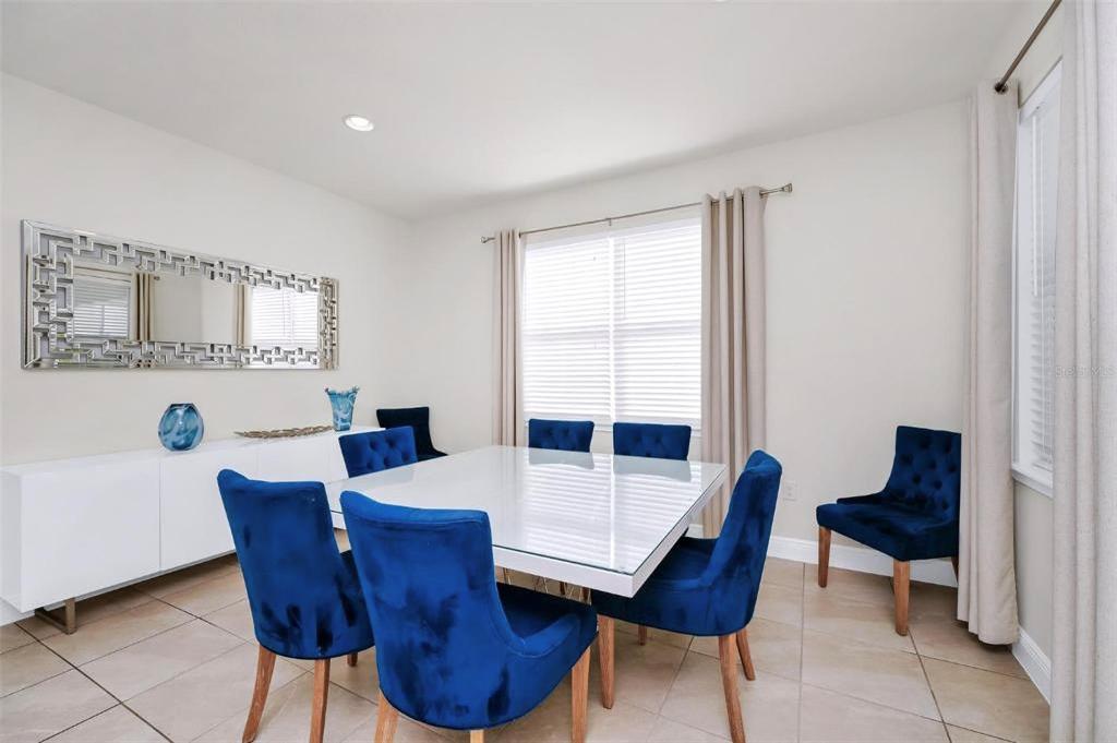 A dining room features a white table, blue velvet chairs, and a large wall mirror — 7727 FAIRFAX DRIVE, KISSIMMEE, FL