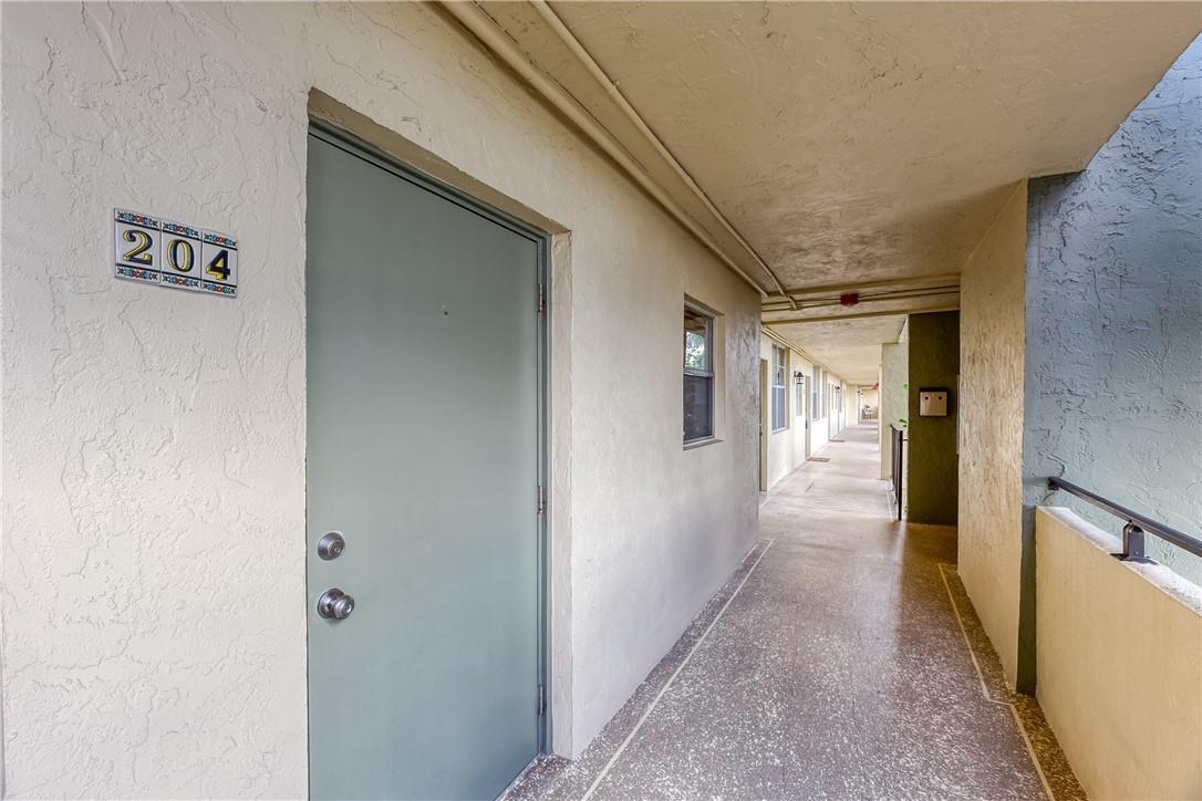 An exterior apartment hallway features a gray door labeled 204 and a concrete walkway — 2400 NE 10th Street # 204, Pompano Beach FL 33062, POMPANO BEACH, FL