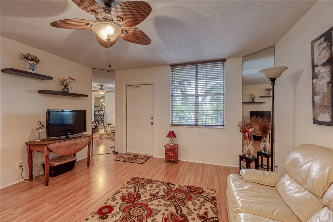 A living room with wood-look flooring, a ceiling fan, a patterned rug, and mirrored walls — 2400 NE 10th Street # 204, Pompano Beach FL 33062, POMPANO BEACH, FL