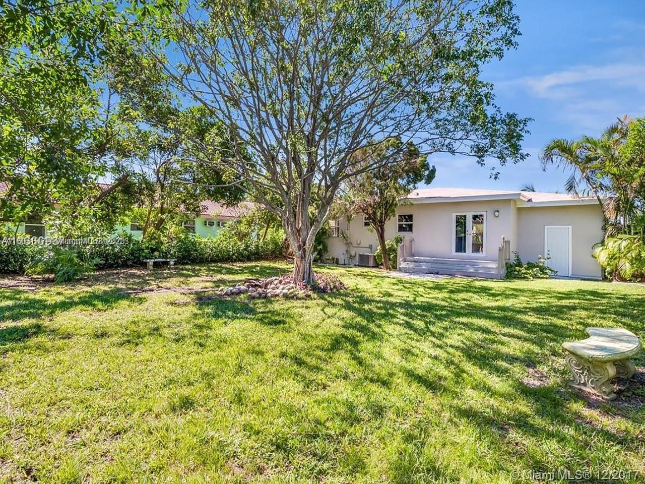 A grassy backyard features a large central tree, a stone bench, and a single-story house — 1231 N 16th Ct, Hollywood FL 33020, HOLLYWOOD, FL