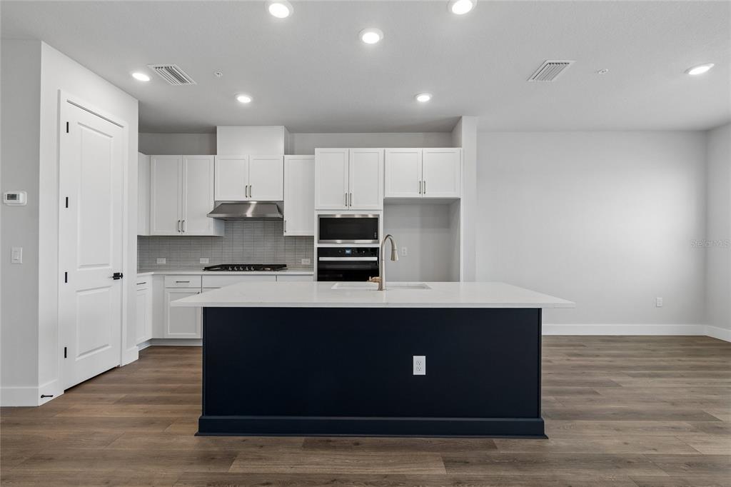 A modern kitchen features white cabinetry, a dark blue island, and light wood flooring — 7227 TIDELAND LANE, SARASOTA, FL