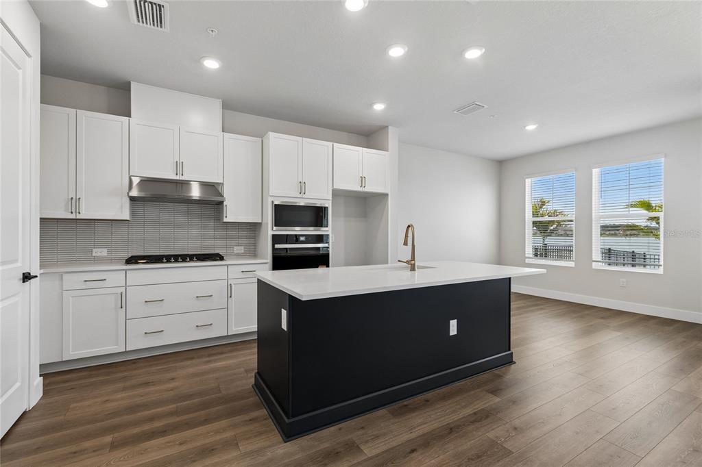 A modern kitchen features white cabinetry, a black island, stainless appliances, and wood-look flooring — 7227 TIDELAND LANE, SARASOTA, FL