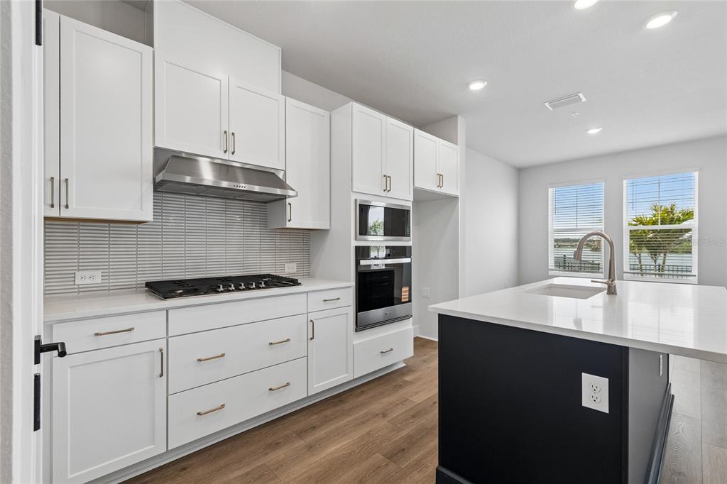 A modern kitchen features white cabinetry, stainless steel appliances, a gas cooktop, and a dark island — 7227 TIDELAND LANE, SARASOTA, FL