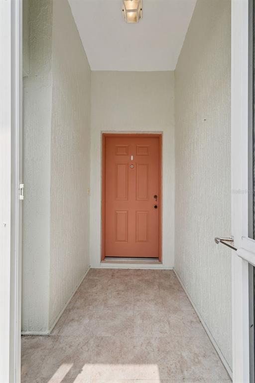 A view of a covered entryway with a terracotta-colored door and light-colored tiled flooring — 472 SWEETWATER WAY, HAINES CITY, FL