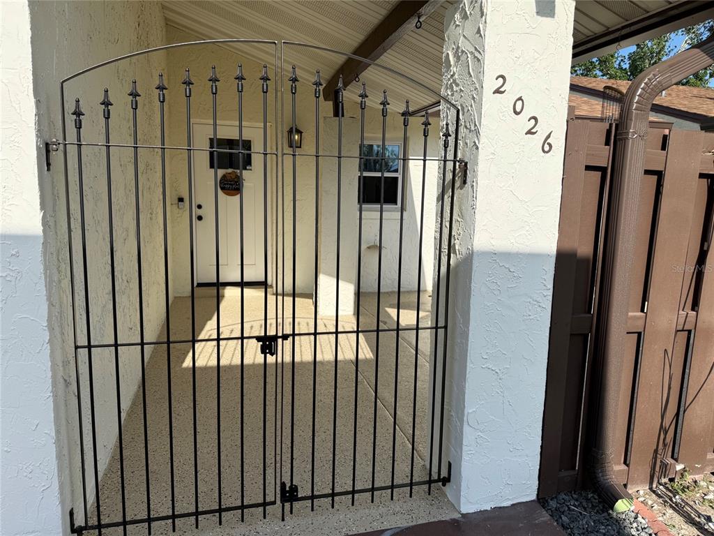A black metal gate secures the entrance to a covered porch with a white door — 2026 KINGS CROSSING SW, WINTER HAVEN, FL