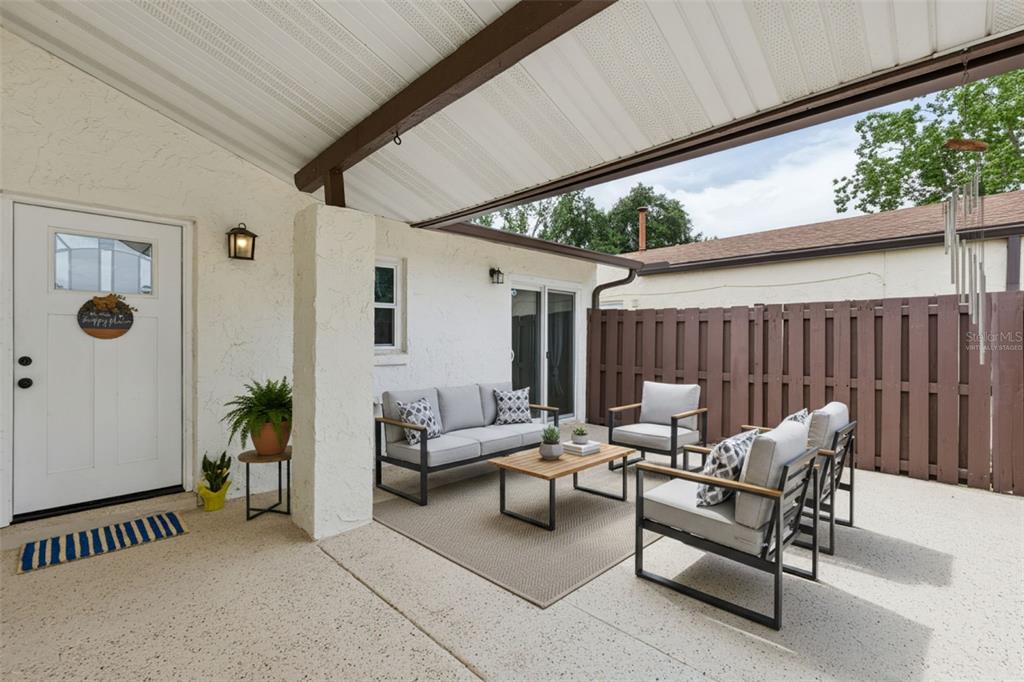 A covered patio features a concrete floor, white stucco walls, and modern outdoor furniture — 2026 KINGS CROSSING SW, WINTER HAVEN, FL