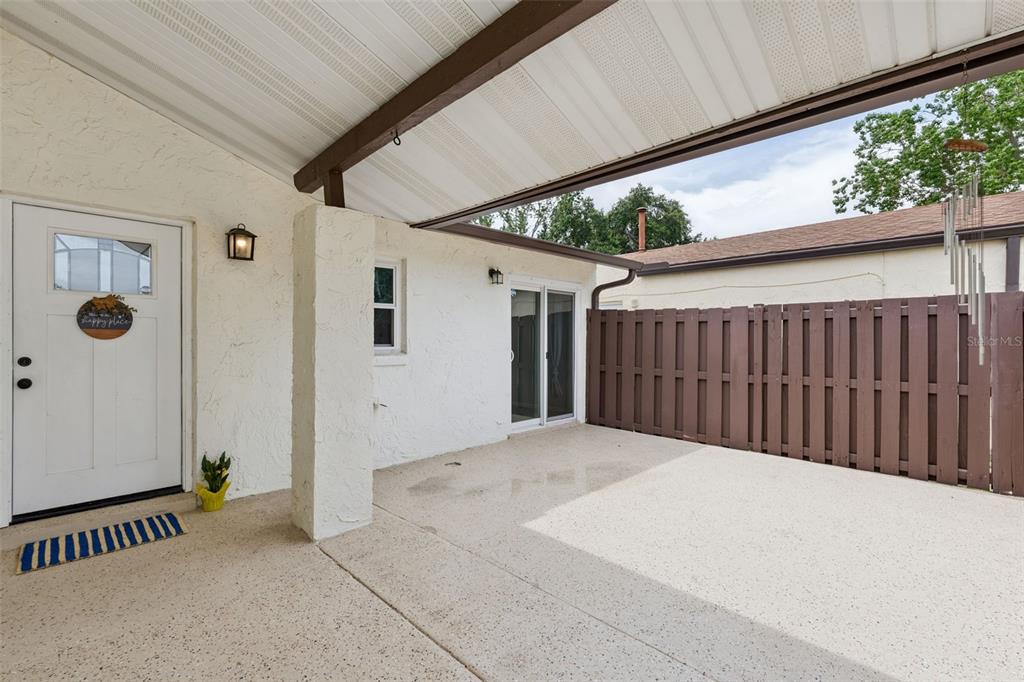 A covered concrete patio features a white door, sliding glass doors, and a brown fence — 2026 KINGS CROSSING SW, WINTER HAVEN, FL
