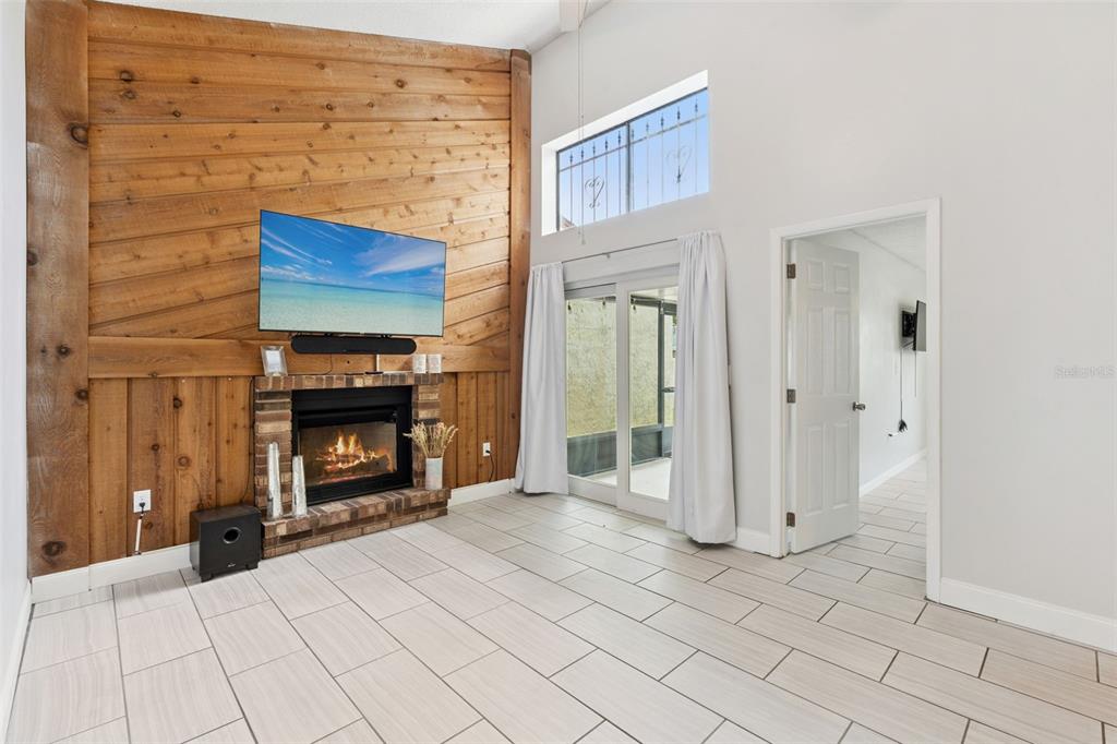 A living room features a wood-paneled accent wall, a brick fireplace, and tile flooring — 2026 KINGS CROSSING SW, WINTER HAVEN, FL