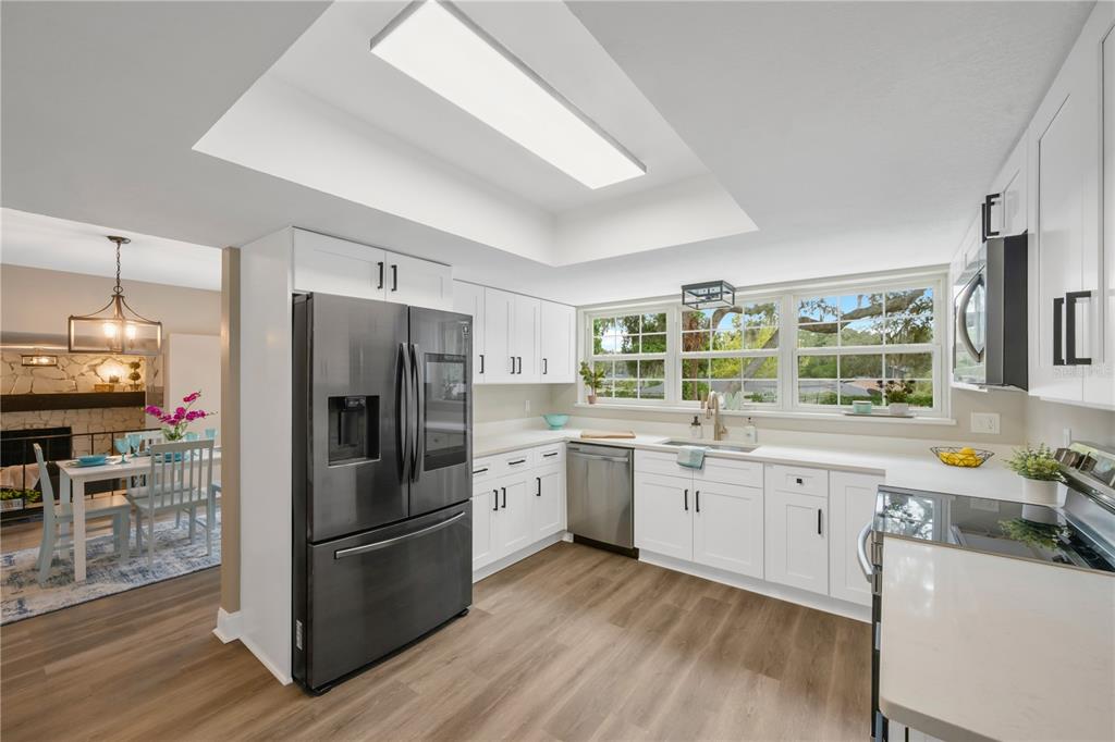 A modern kitchen features white cabinets, stainless steel appliances, and wood-look flooring under a skylight — 122 WINDY PLACE, BRANDON, FL