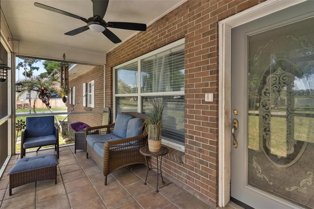 A screened-in brick porch features a ceiling fan, wicker furniture, and a decorative glass door — 14407 LAKE JUNIETTA DRIVE, TAVARES, FL