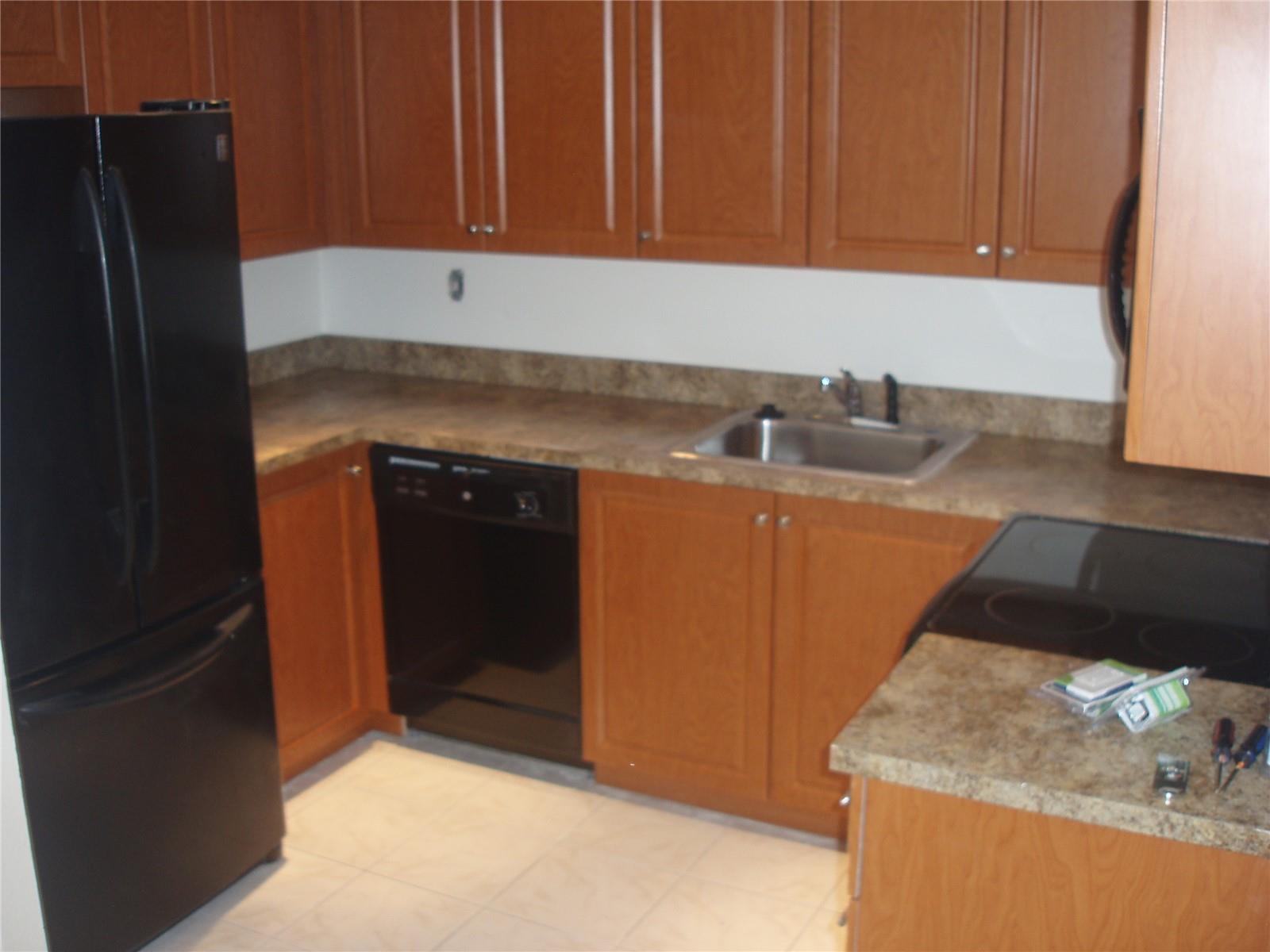 A kitchen features wood cabinets, a black refrigerator, a dishwasher, and a laminate countertop — 8028 SW 17th Place, Davie FL 33324, DAVIE, FL