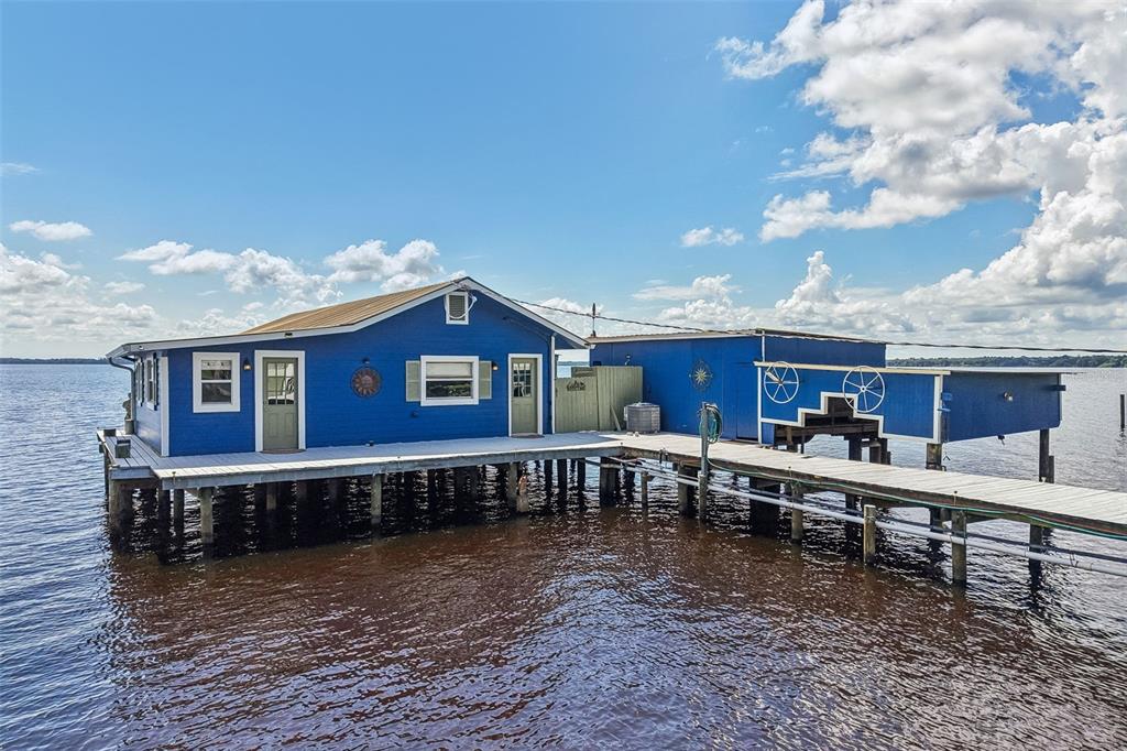 A blue house on stilts sits above the water, connected to a dock — 21 S LAKE STREET, CRESCENT CITY, FL