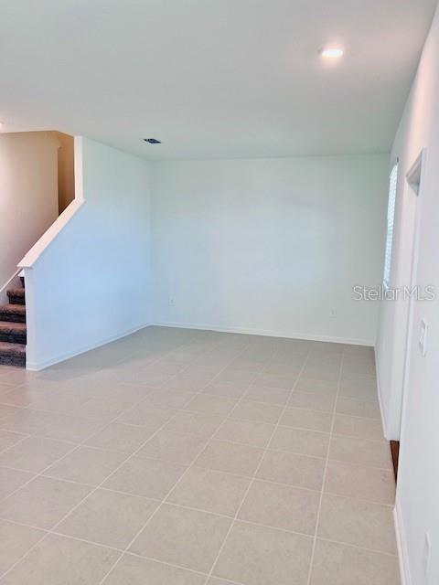 An empty room with light-colored tile flooring, white walls, and a staircase on the left — 2639 CANDIED APPLE ALLEY, KISSIMMEE, FL