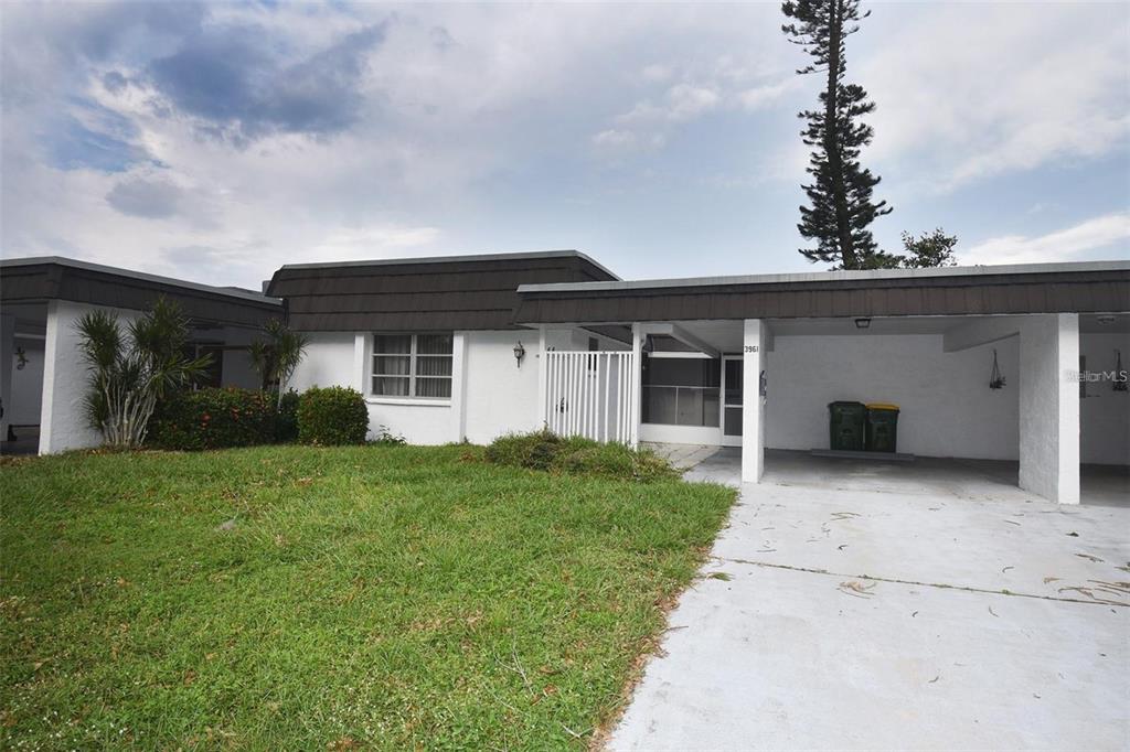 A white single-story house features a flat roof, a carport, and a small front lawn — 3961 ASHWOOD LANE UNIT 44, SARASOTA, FL
