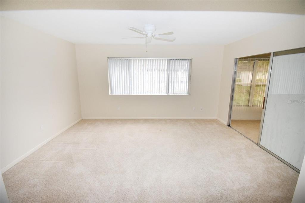 An empty room with beige carpet, a ceiling fan, a window with blinds, and sliding doors — 3961 ASHWOOD LANE UNIT 44, SARASOTA, FL