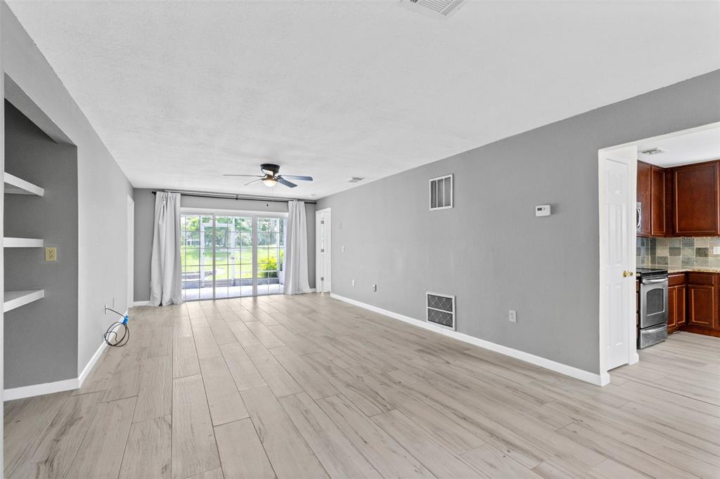 An open living room with light wood-look tile flooring, gray walls, and sliding glass doors — 4102 CLUBSIDE DRIVE, LONGWOOD, FL