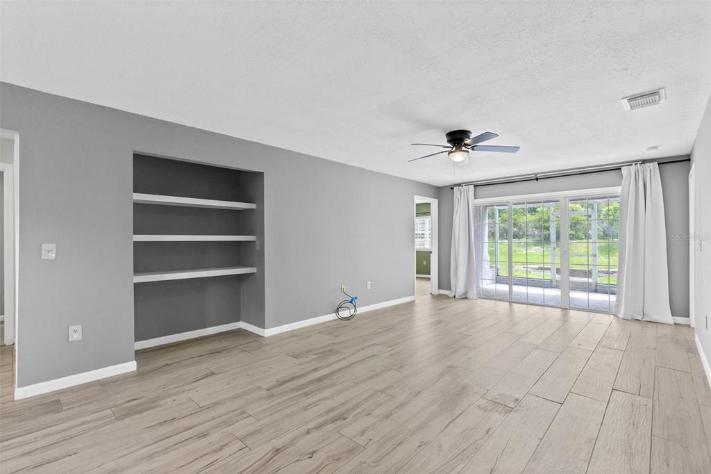 A living room with light wood-look tile flooring, gray walls, built-in shelves, and sliding glass doors — 4102 CLUBSIDE DRIVE, LONGWOOD, FL