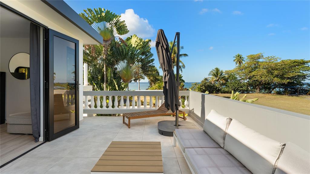 A balcony with a sofa, lounge chair, umbrella, and ocean view overlooks a grassy yard — 473 Bo. Ensenada CARR 413 KM HM 0.7, RINCON, PR