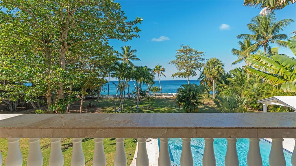 A balcony with a stone railing overlooks a swimming pool, lawn, palm trees, and ocean — 473 Bo. Ensenada CARR 413 KM HM 0.7, RINCON, PR