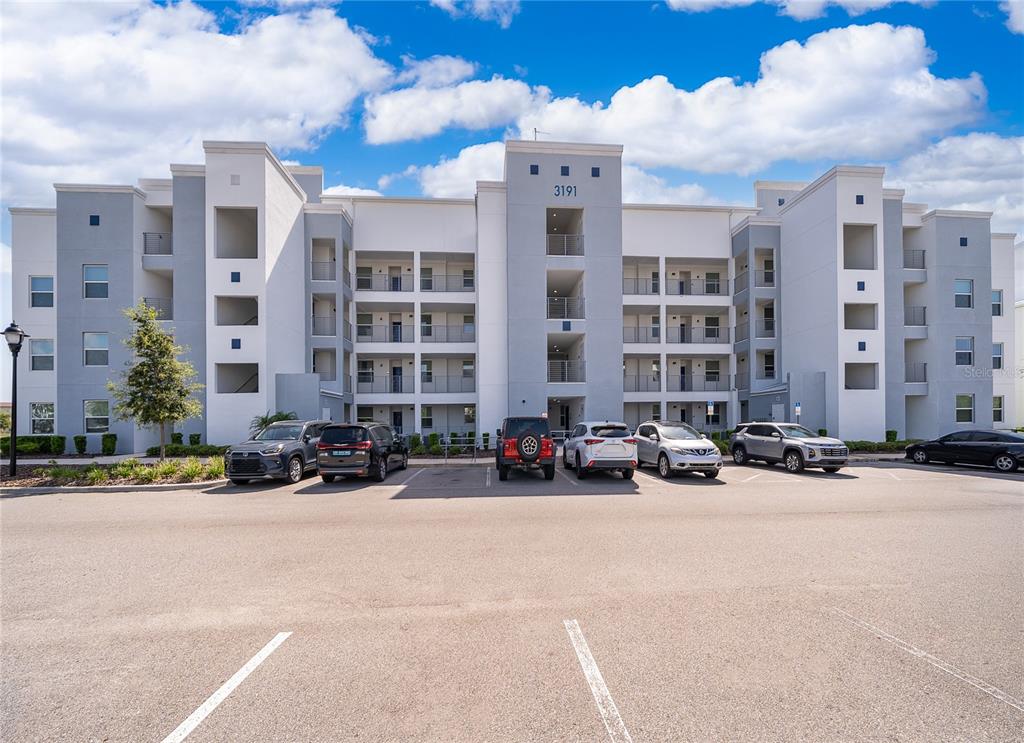 A multi-story apartment building with a parking lot in the foreground under a cloudy sky — 3191 PARADOX CIRCLE UNIT 208, KISSIMMEE, FL