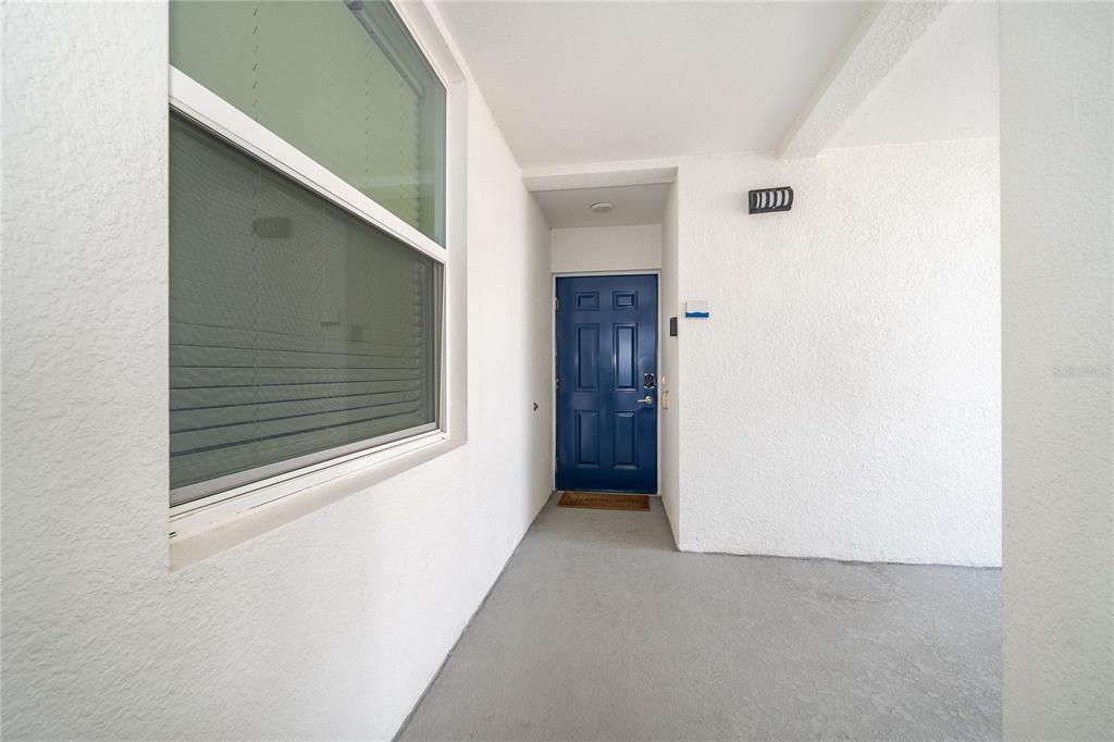 A covered entryway features a blue front door, a window with blinds, and concrete flooring — 3191 PARADOX CIRCLE UNIT 208, KISSIMMEE, FL