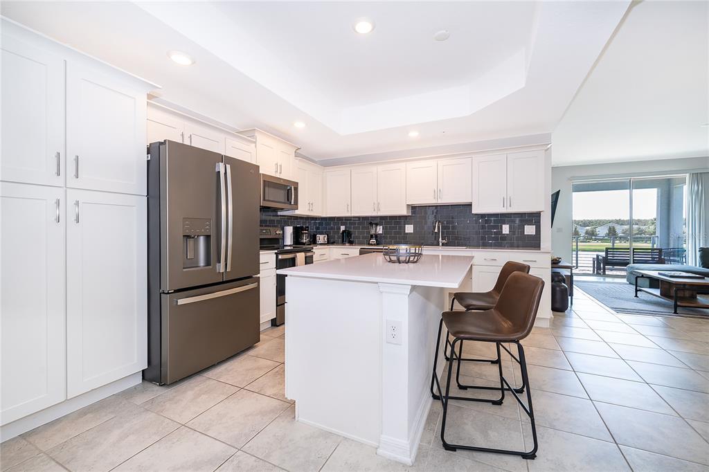 A kitchen with white cabinets, stainless steel appliances, a center island, and dark tile backsplash — 3191 PARADOX CIRCLE UNIT 208, KISSIMMEE, FL