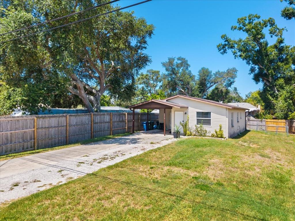 A single-story house with a carport, concrete driveway, and wooden fence on a sunny day — 4050 ROCKEFELLER AVENUE, SARASOTA, FL