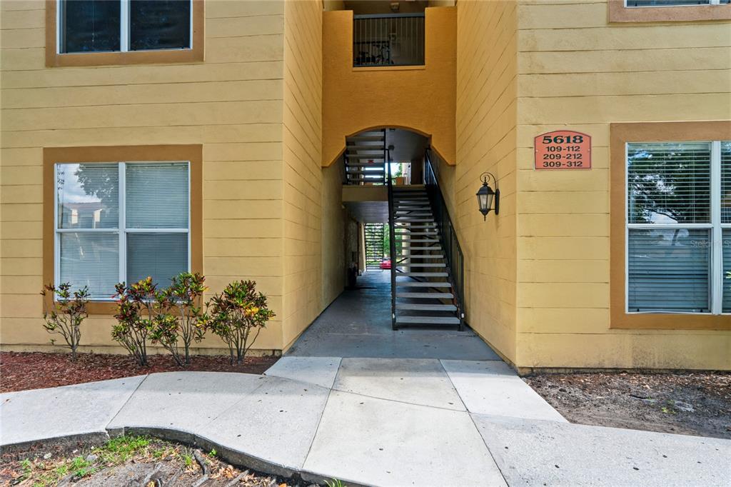 An exterior view of a yellow apartment building with an open-air staircase and walkway — 5618 PINNACLE HEIGHTS CIRCLE UNIT 312, TAMPA, FL