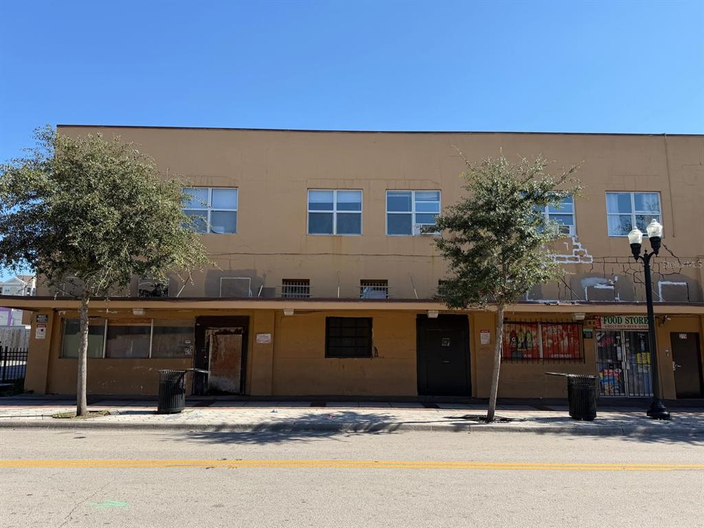 A two-story tan commercial building with a ground-level food store and two trees in front — 221 S PARRAMORE AVENUE UNIT 7A, ORLANDO, FL