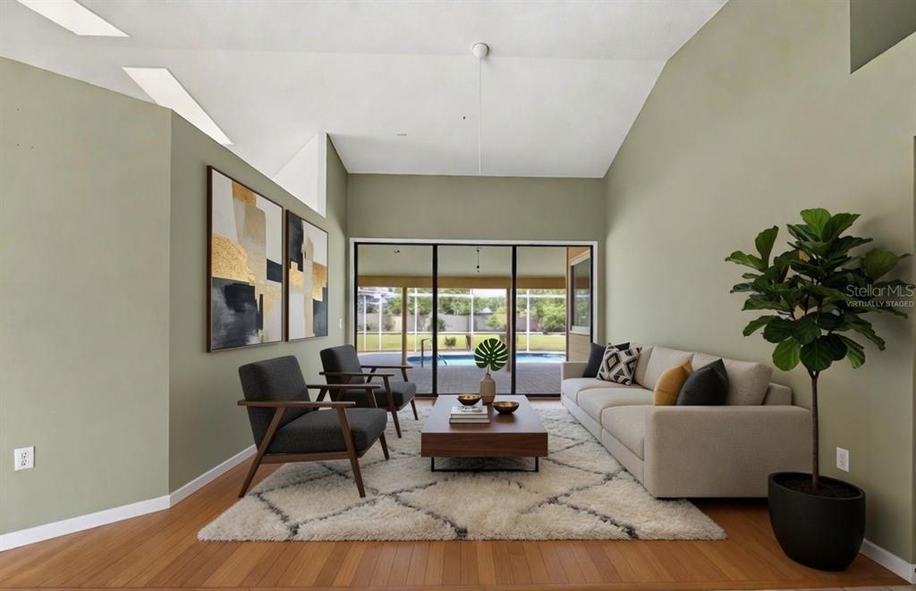 A virtually staged living room features light green walls, wood flooring, and sliding glass doors — 8432 PALM LAKES COURT, SARASOTA, FL