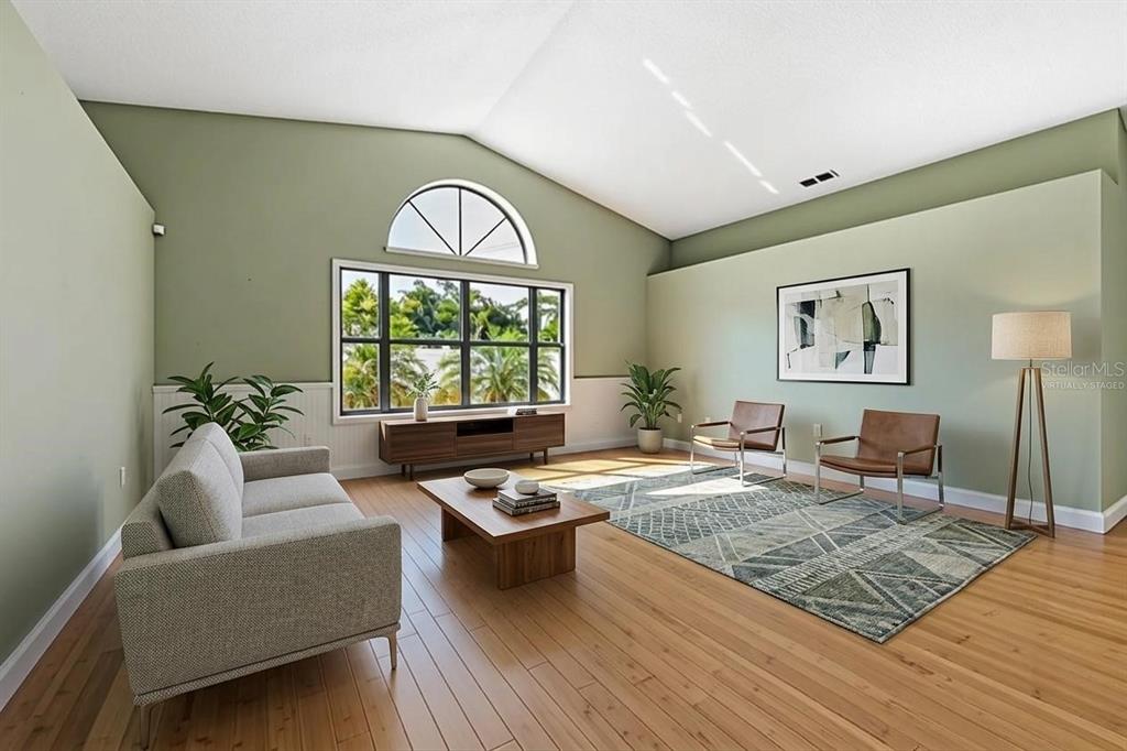 A living room with vaulted ceilings, light green walls, hardwood floors, and a large window — 8432 PALM LAKES COURT, SARASOTA, FL