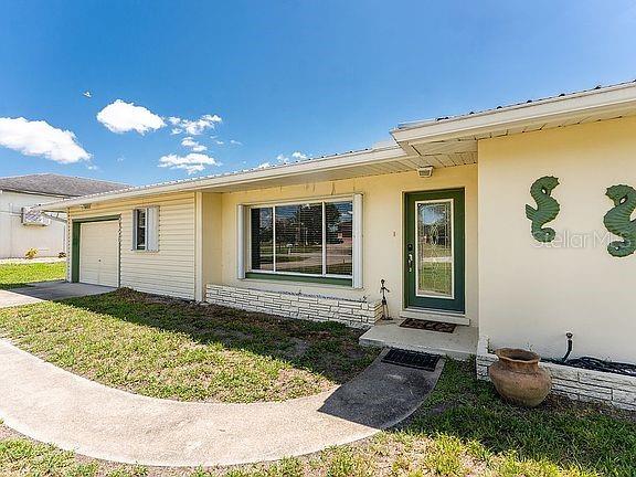 The exterior of a single-story house features light yellow siding, a front door, and windows — 3420 SANTA CLARA DRIVE, PUNTA GORDA, FL