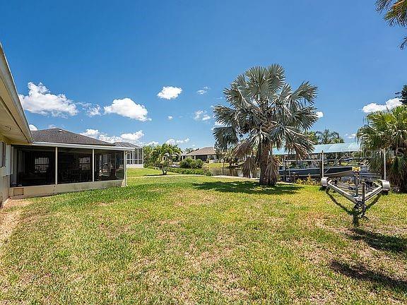 A grassy backyard features a screened-in patio, a large palm tree, and a boat lift — 3420 SANTA CLARA DRIVE, PUNTA GORDA, FL