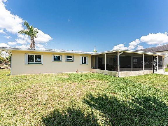 The rear exterior of a single-story house features a screened-in porch and a grassy yard — 3420 SANTA CLARA DRIVE, PUNTA GORDA, FL