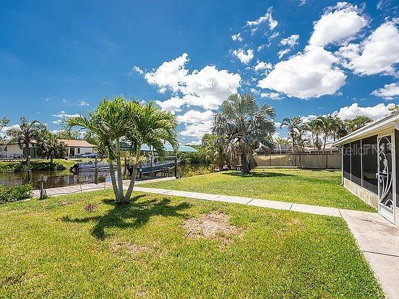 A grassy backyard features a palm tree, a concrete walkway, and a view of a canal — 3420 SANTA CLARA DRIVE, PUNTA GORDA, FL