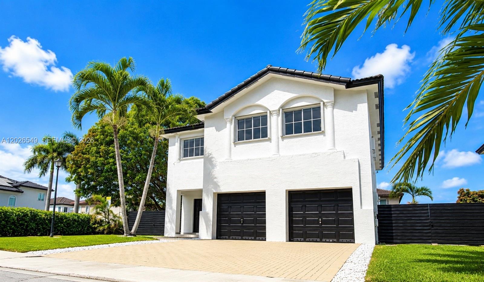 A two-story white house features a two-car garage and palm trees under a blue sky — 14407 SW 158th Path, Miami FL 33196, MIAMI, FL