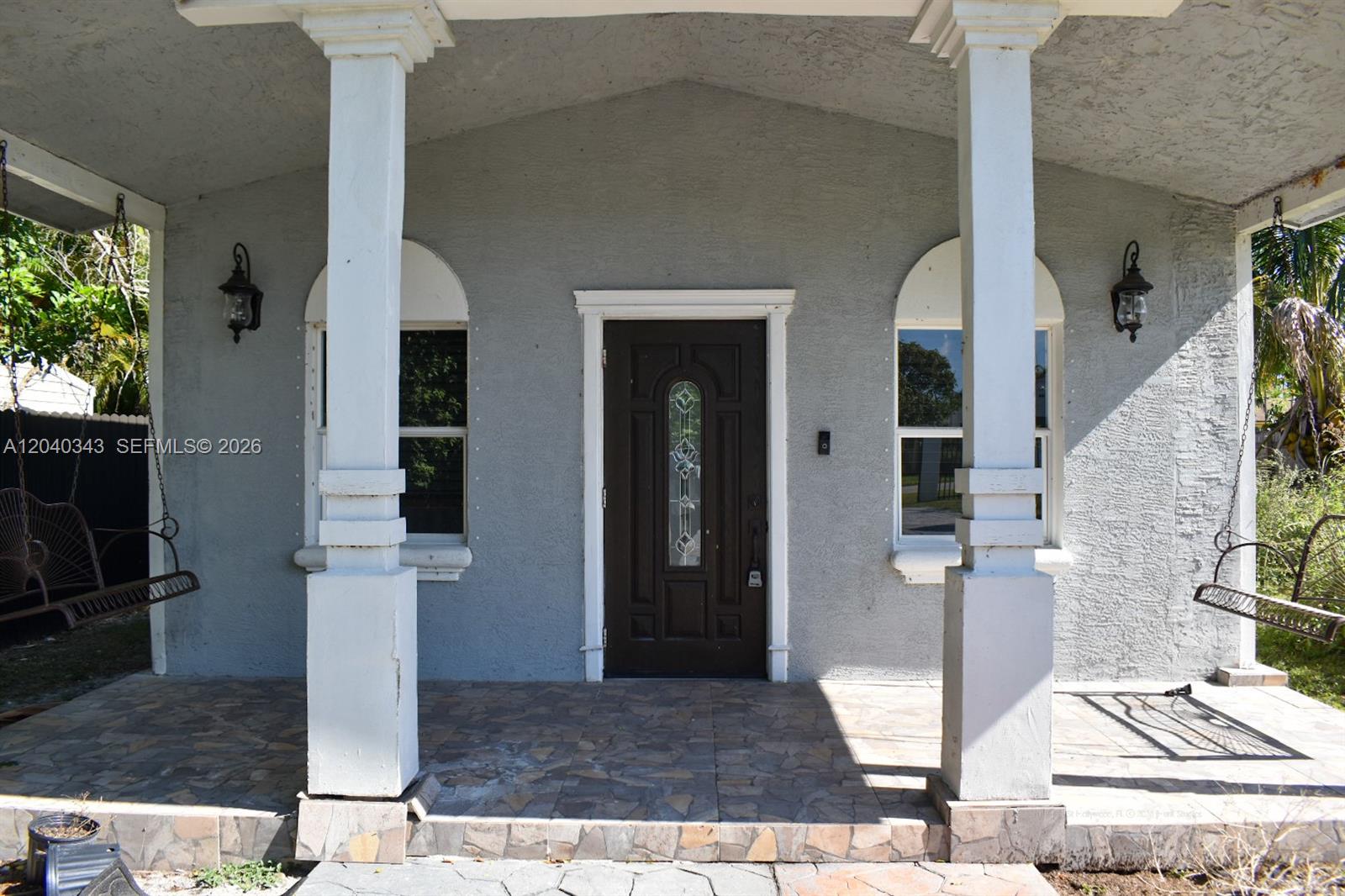 A covered front porch features two hanging swings, white columns, and a dark entry door — 2218 N Harding St # 0, Hollywood FL 33020, HOLLYWOOD, FL