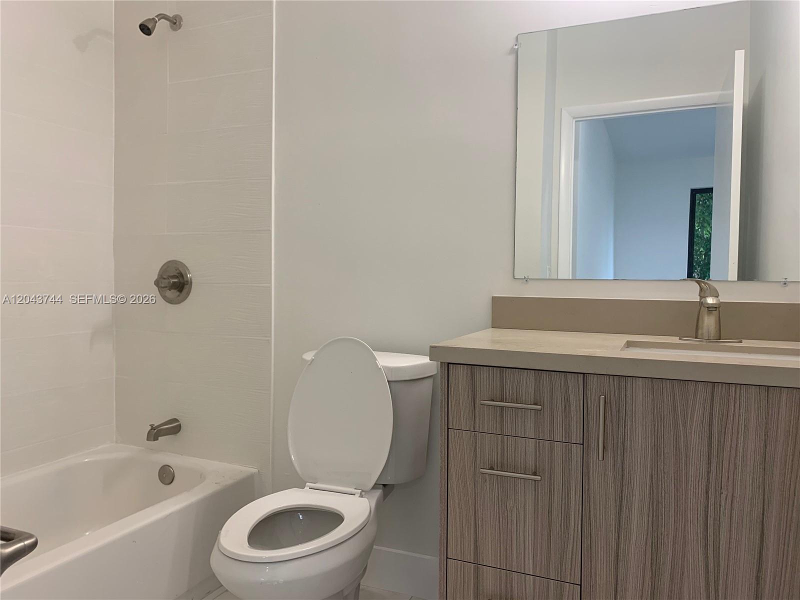 A bathroom features a white bathtub, a toilet, and a wood-grain vanity with a mirror — 211 NW 7th Ct # B, Hallandale Beach FL 33009, HALLANDALE BEACH, FL