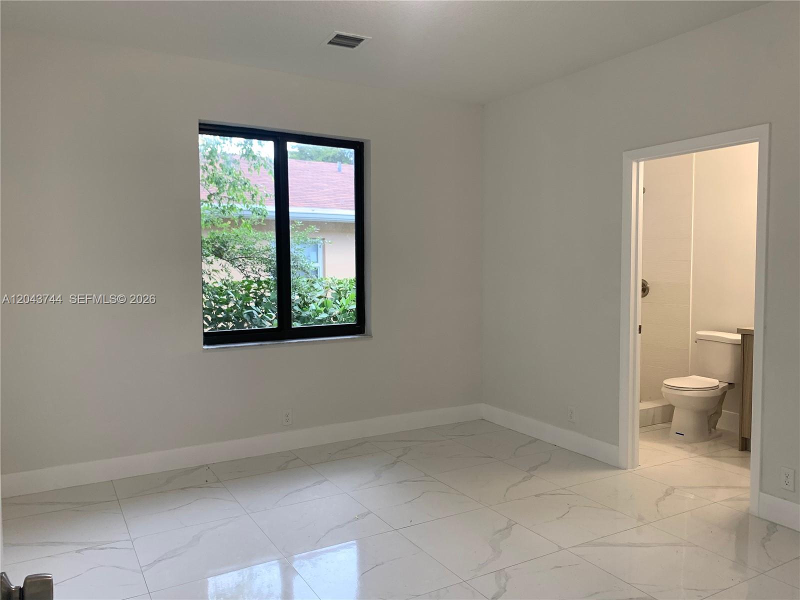 A bedroom with white marble-look tile flooring, a window, and an attached bathroom — 211 NW 7th Ct # B, Hallandale Beach FL 33009, HALLANDALE BEACH, FL