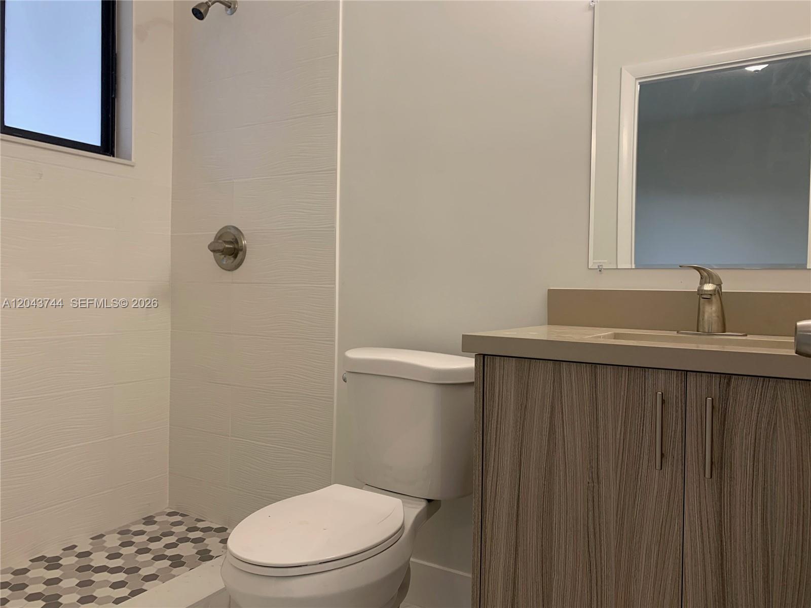 A bathroom features a walk-in shower with patterned tile, a toilet, and a wood-grain vanity — 211 NW 7th Ct # B, Hallandale Beach FL 33009, HALLANDALE BEACH, FL