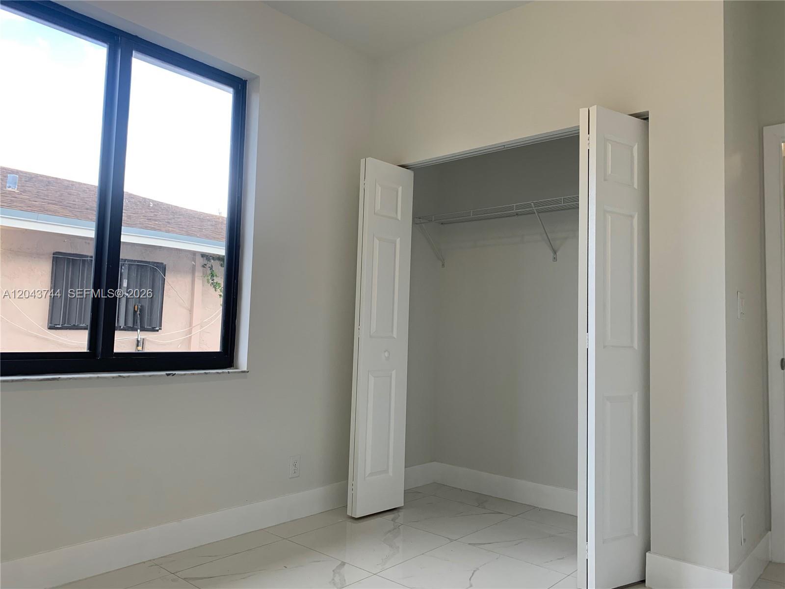 A room with white tile floors, a large window, and an open closet with shelving — 211 NW 7th Ct # B, Hallandale Beach FL 33009, HALLANDALE BEACH, FL