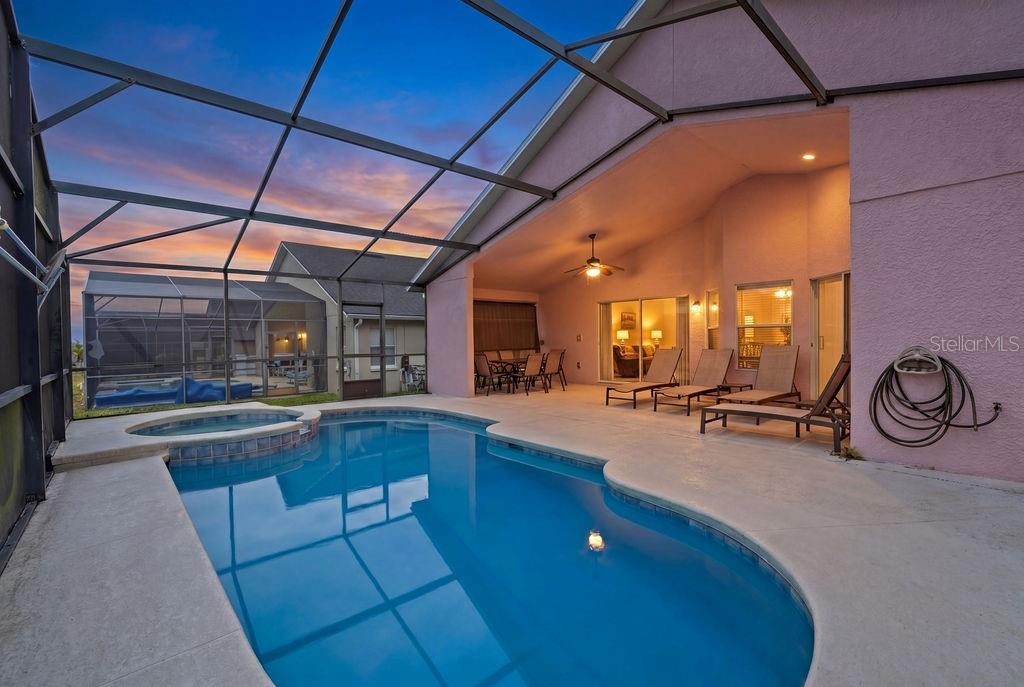 A screened-in patio features a swimming pool, hot tub, and lounge chairs at sunset — 620 OLD BRIDGE CIRCLE, DAVENPORT, FL