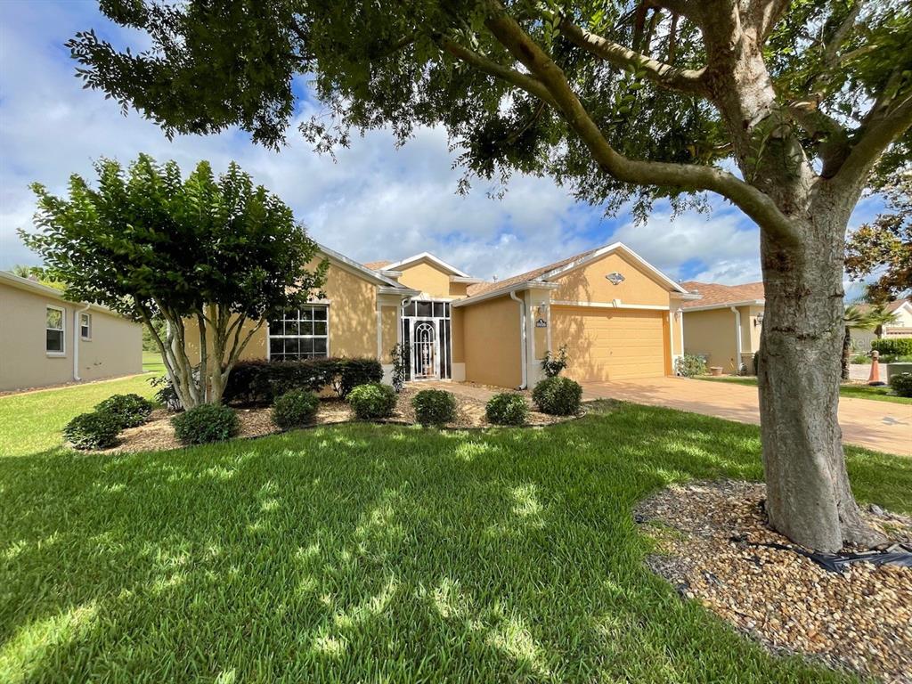 A single-story house with a tan exterior, two-car garage, and a large tree in front — 16026 SW 14TH AVENUE ROAD, OCALA, FL